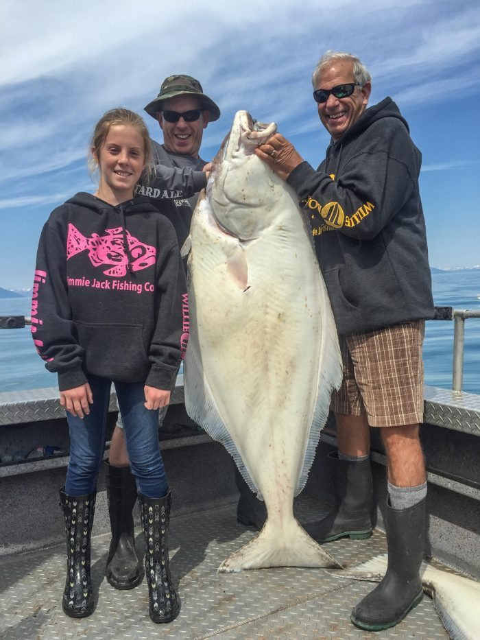 Two adult men and young woman holding a large halibut