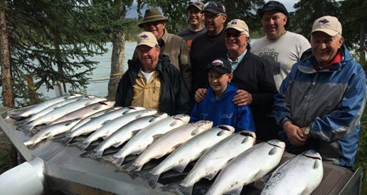 Group of men and young boy standing with a dozen salmon.