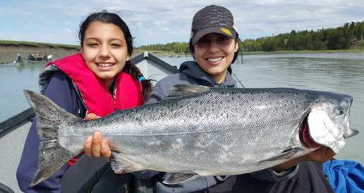 Two women holding a large salmon on a fishing boat