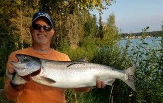 A man holding a massive king salmon on the banks of the Kenai River.
