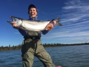 A jubilant female angler proudly displays her large salmon while fall fishing on the Kenai River in Alaska.