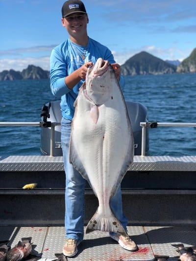 A happy fisherman holds up a massive halibut while enjoying an Alaska fishing charter trip.