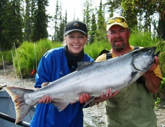 An avid angler and her guide display a massive king salmon during the Alaskan fishing season.