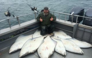 A joyous angler squats behind a large haul of halibut while giving a double thumbs-up pose.