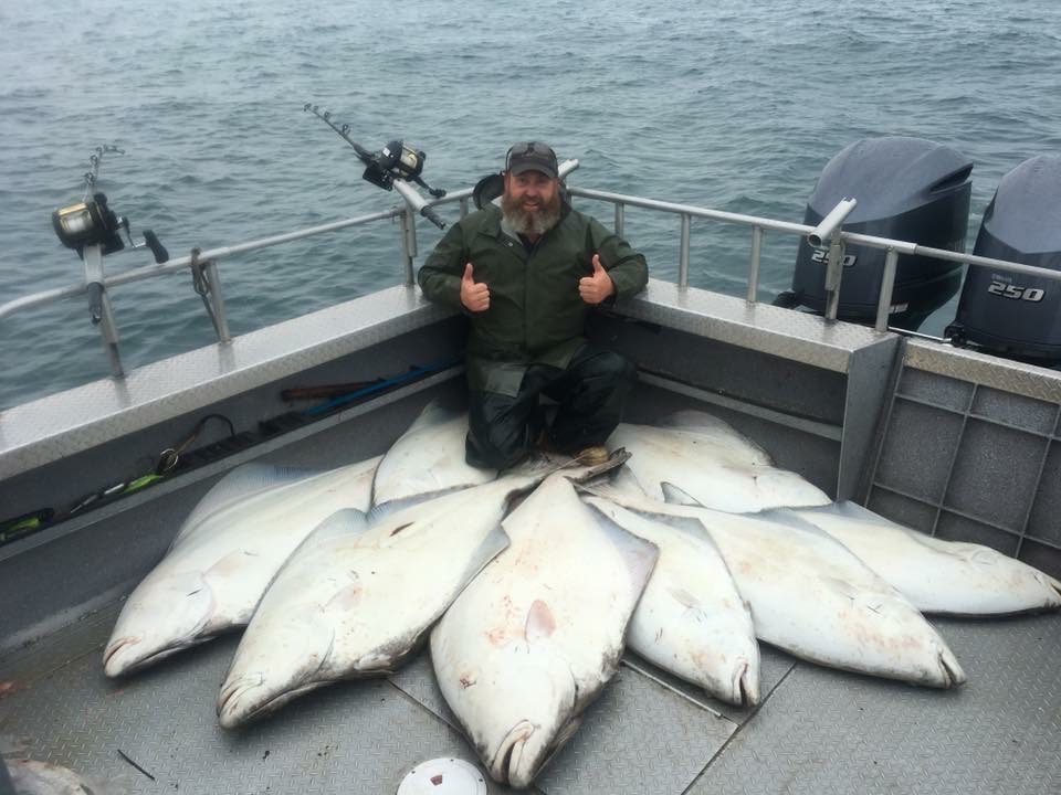 A joyous angler squats behind a large haul of halibut while giving a double thumbs-up pose.