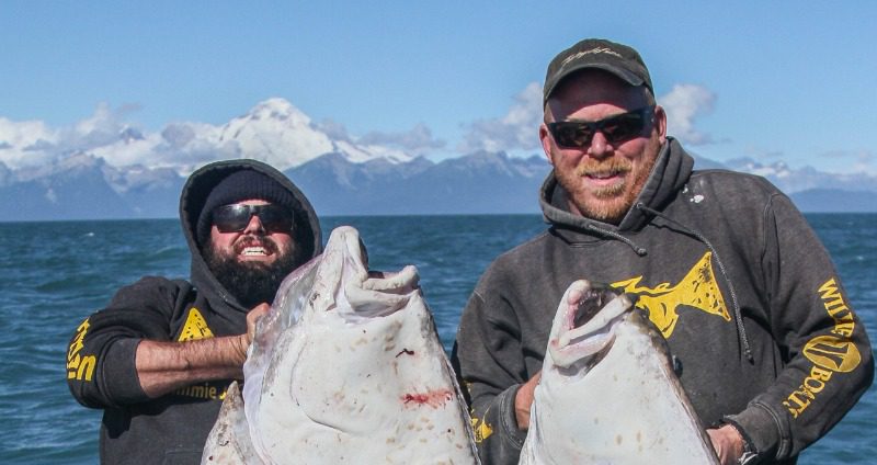 Two avid anglers holding large halibut in their Jimmie Jack Gear fishing apparel. 