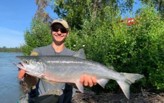 Salmon Fishing in Alaska: An avid angler smiles while holding a large salmon on the Kenai River.