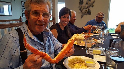 Alaska Luxury Fishing Lodge: A guest of the SeaScape Lodge smiles while holding a large crab leg at the dinner table.