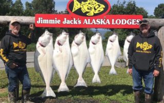 Halibut Fishing Trips Homer Alaska: Two halibut fishermen smile with a large haul of massive halibut hanging behind them.