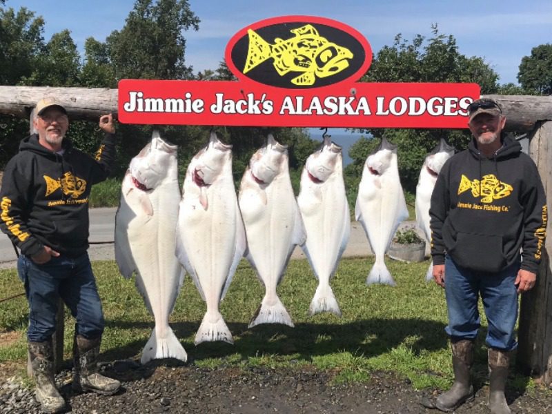 Halibut Fishing Trips Homer Alaska: Two halibut fishermen smile with a large haul of massive halibut hanging behind them.