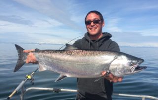 Combo Fishing Trip: An angler smiles while holding a large salmon caught on an Alaska fishing charter.