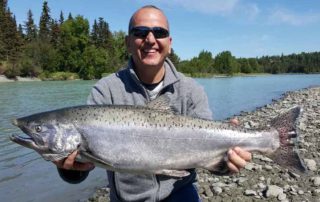 Kasilof River Fishing: A happy angler holds a massive salmon along the Kasilof River in Alaska.